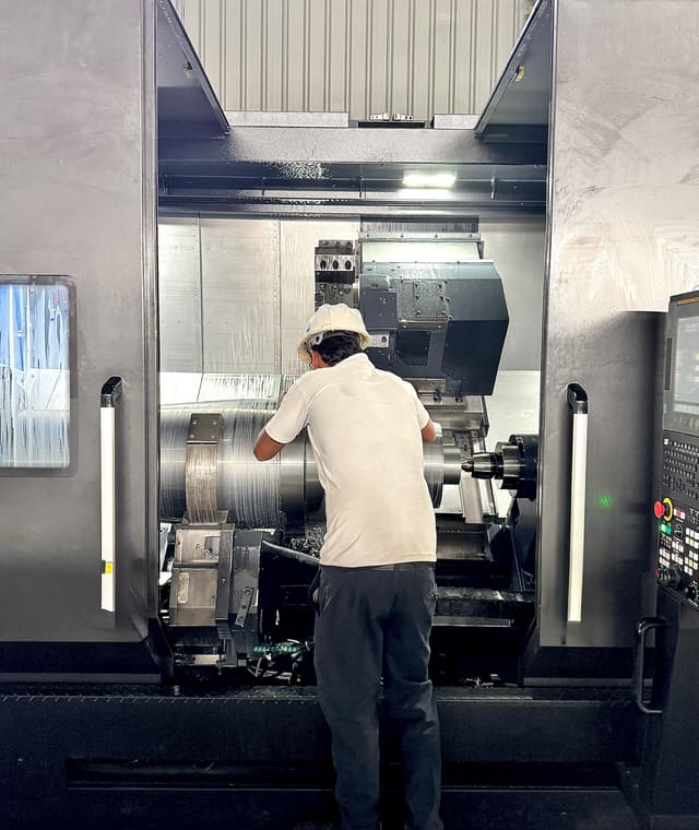 A shaft turning between centres on a CNC lathe, swarf breaking off the tool.