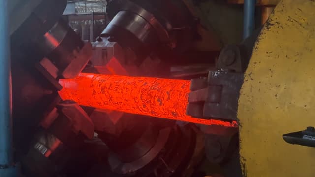 A long workpiece at forging heat held by the manipulator as the radial forge works along it.