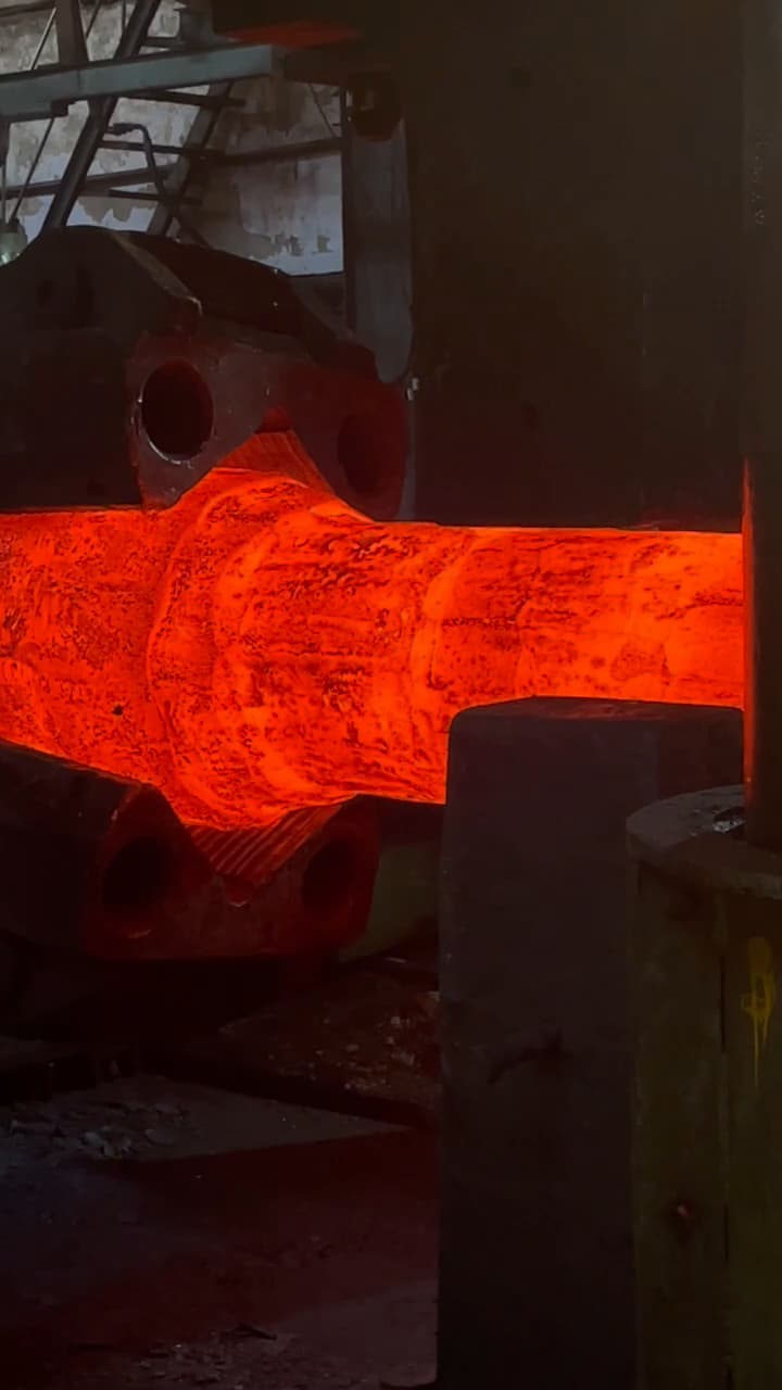 A bar at forging heat being cogged down under the press between flat dies.