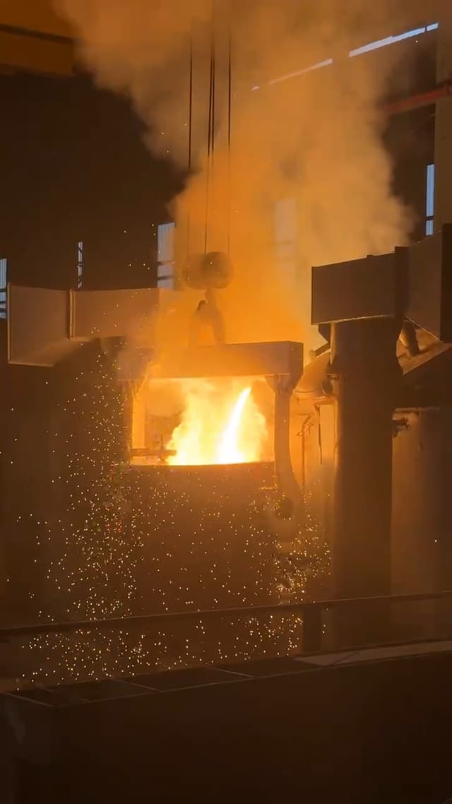 Molten steel pouring from the furnace into the mould, sparks rising.