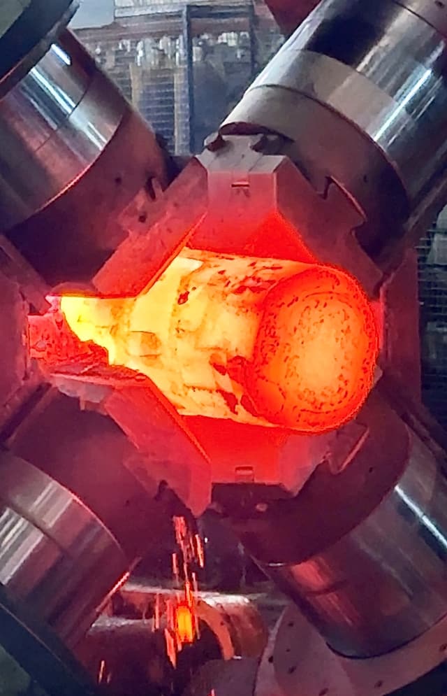 Four dies closed around a billet at forging heat inside the radial forge.